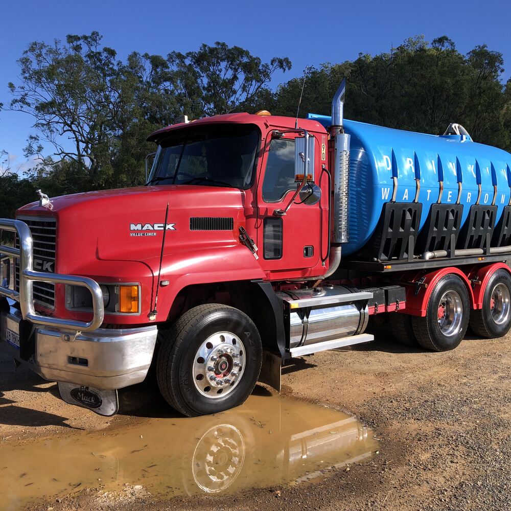 Red Mack water truck with a large blue tank parked on a dirt site, used for local water delivery around Kilcoy and the Somerset region